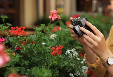 Photo of Young woman with camera taking photobeautiful flowers on city street, closeup. Interesting hobby