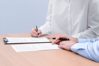 Photo of Businesspeople signing contract at wooden table, closeup of hands