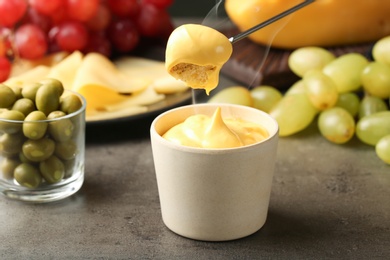 Photo of Piece of bread over bowl with delicious cheese fondue on gray table