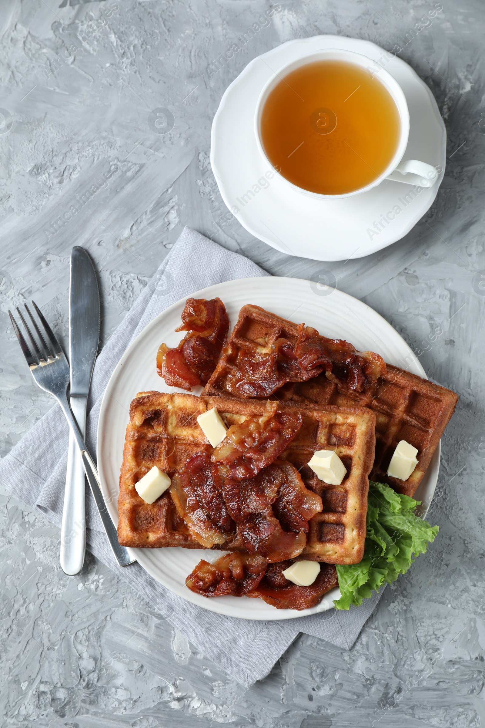 Photo of Delicious Belgium waffles served with fried bacon and butter on grey table, flat lay