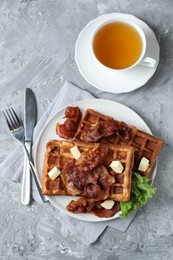 Photo of Delicious Belgium waffles served with fried bacon and butter on grey table, flat lay