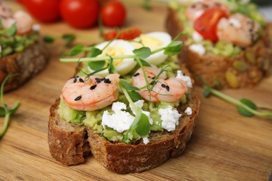 Photo of Delicious sandwiches with guacamole, shrimps and microgreens on wooden table, closeup