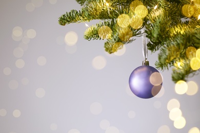 Beautiful Christmas ball hanging on fir tree branch against light background, space for text. Bokeh effect