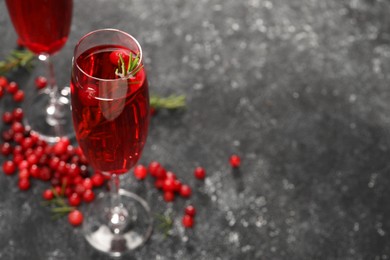 Photo of Tasty cranberry cocktail with rosemary in glasses on gray table, closeup. Space for text
