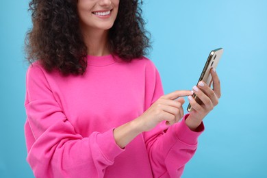 Woman sending message via smartphone on light blue background, closeup