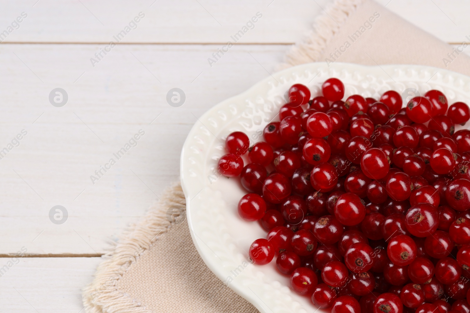 Photo of Plate with ripe red currants on white wooden table, closeup. Space for text