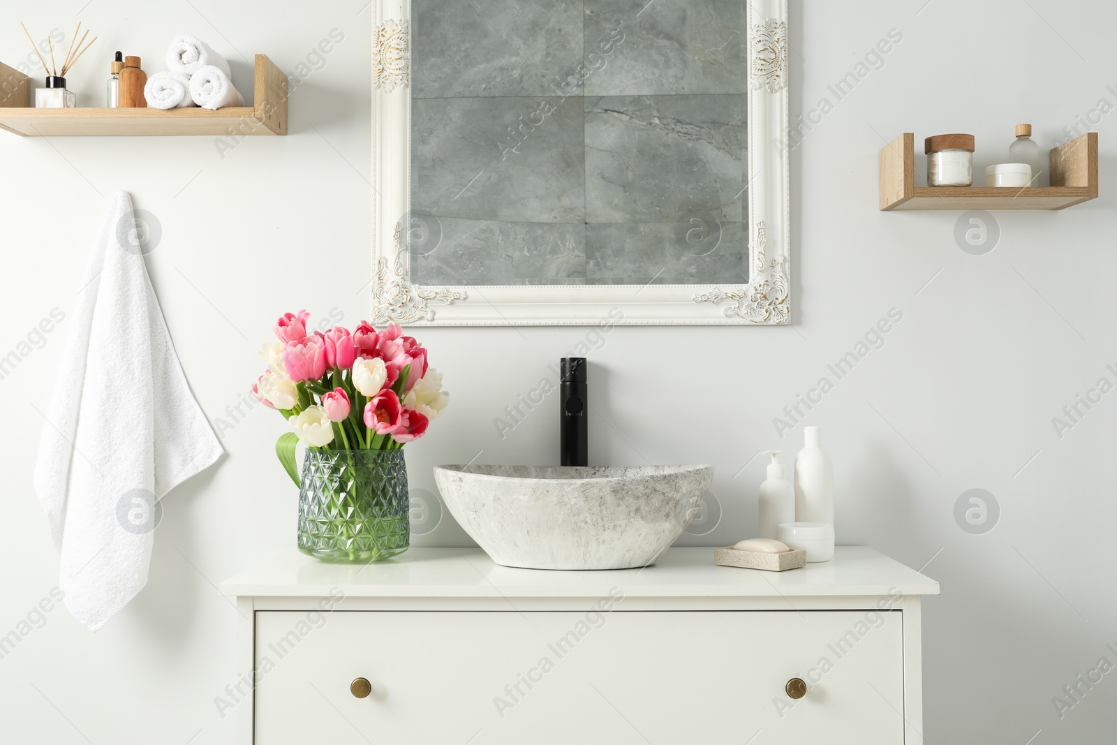 Photo of Vase with beautiful pink tulips and toiletries near sink in bathroom