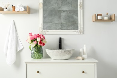 Vase with beautiful pink tulips and toiletries near sink in bathroom