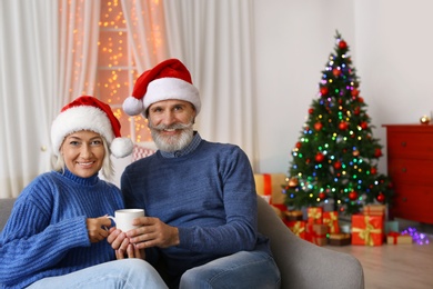 Photo of Happy couple in Santa hats celebrating Christmas at home