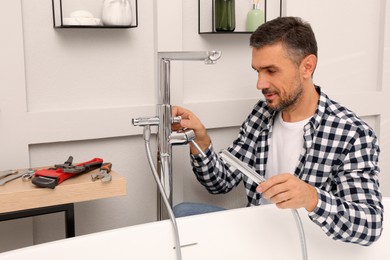 Man installing water tap with shower head in bathroom