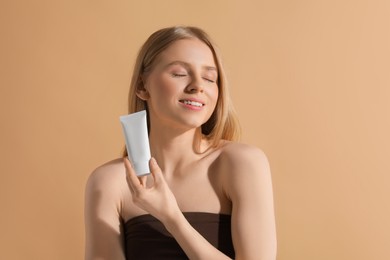 Photo of Beautiful young woman holding sun protection cream on beige background