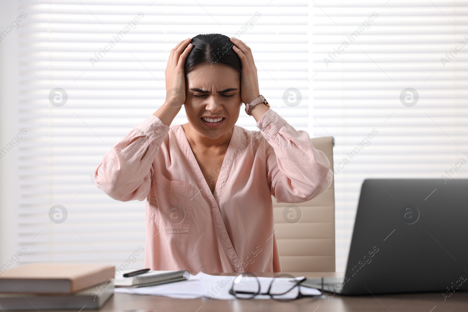 Photo of Young woman suffering from headache at wooden table in office