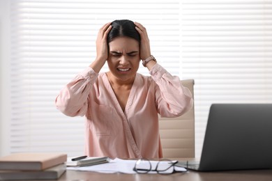 Young woman suffering from headache at wooden table in office