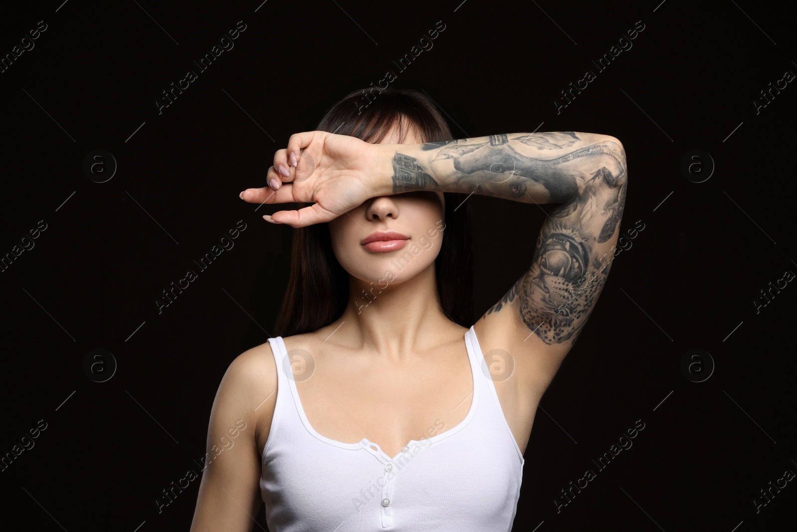 Photo of Beautiful woman with tattoos on arm against black background