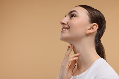 Smiling woman touching her chin on beige background. Space for text