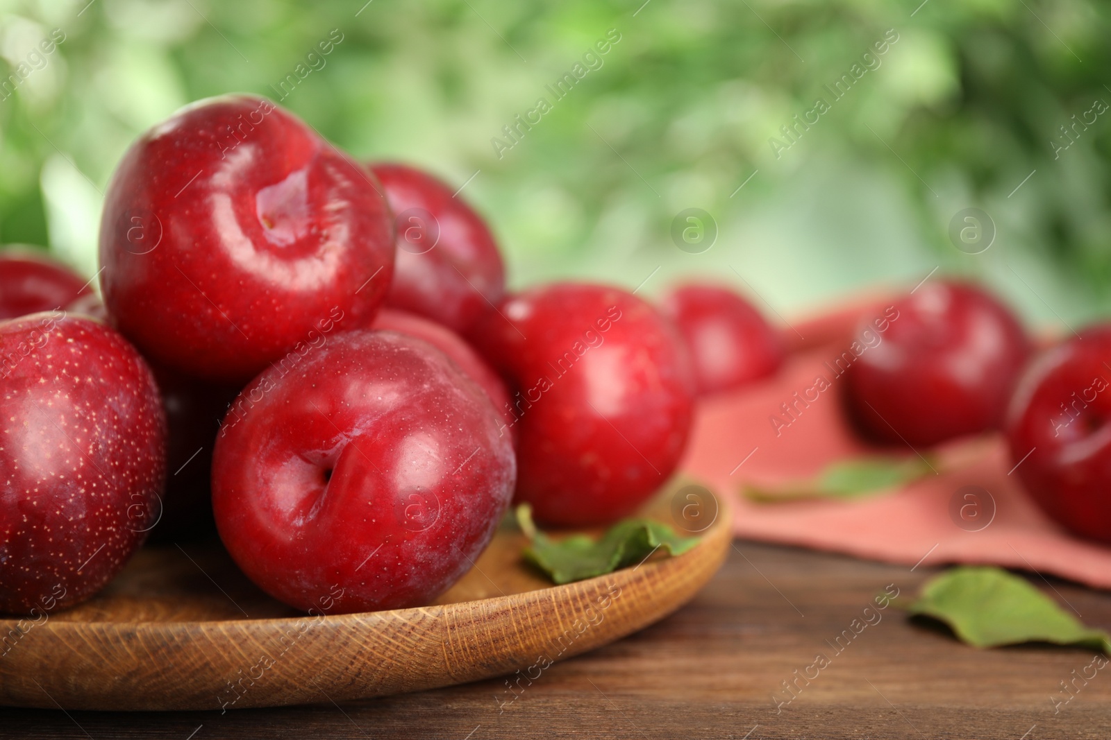 Photo of Delicious ripe plums on wooden table against blurred background, closeup. Space for text