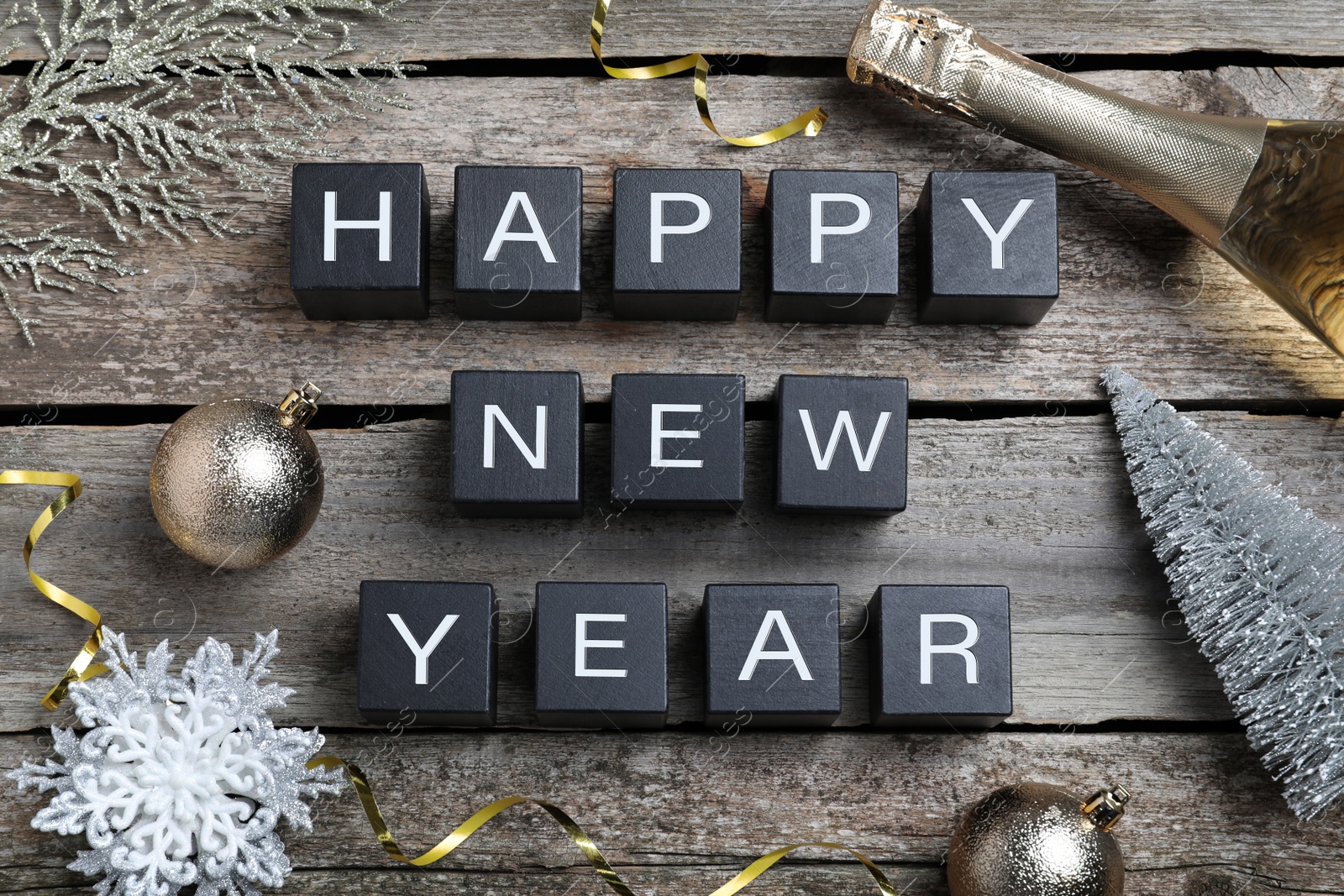Photo of Happy New Year greeting card. Phrase made with cubes and festive decor on wooden background, flat lay