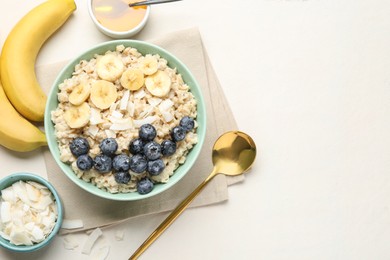 Photo of Tasty oatmeal with banana, blueberries, coconut flakes and honey served in bowl on beige table, flat lay. Space for text