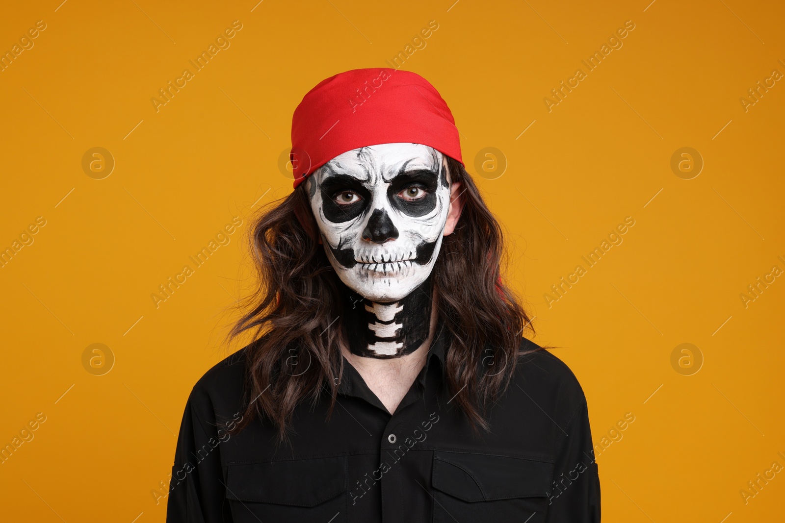 Photo of Man in scary pirate costume with skull makeup on orange background. Halloween celebration