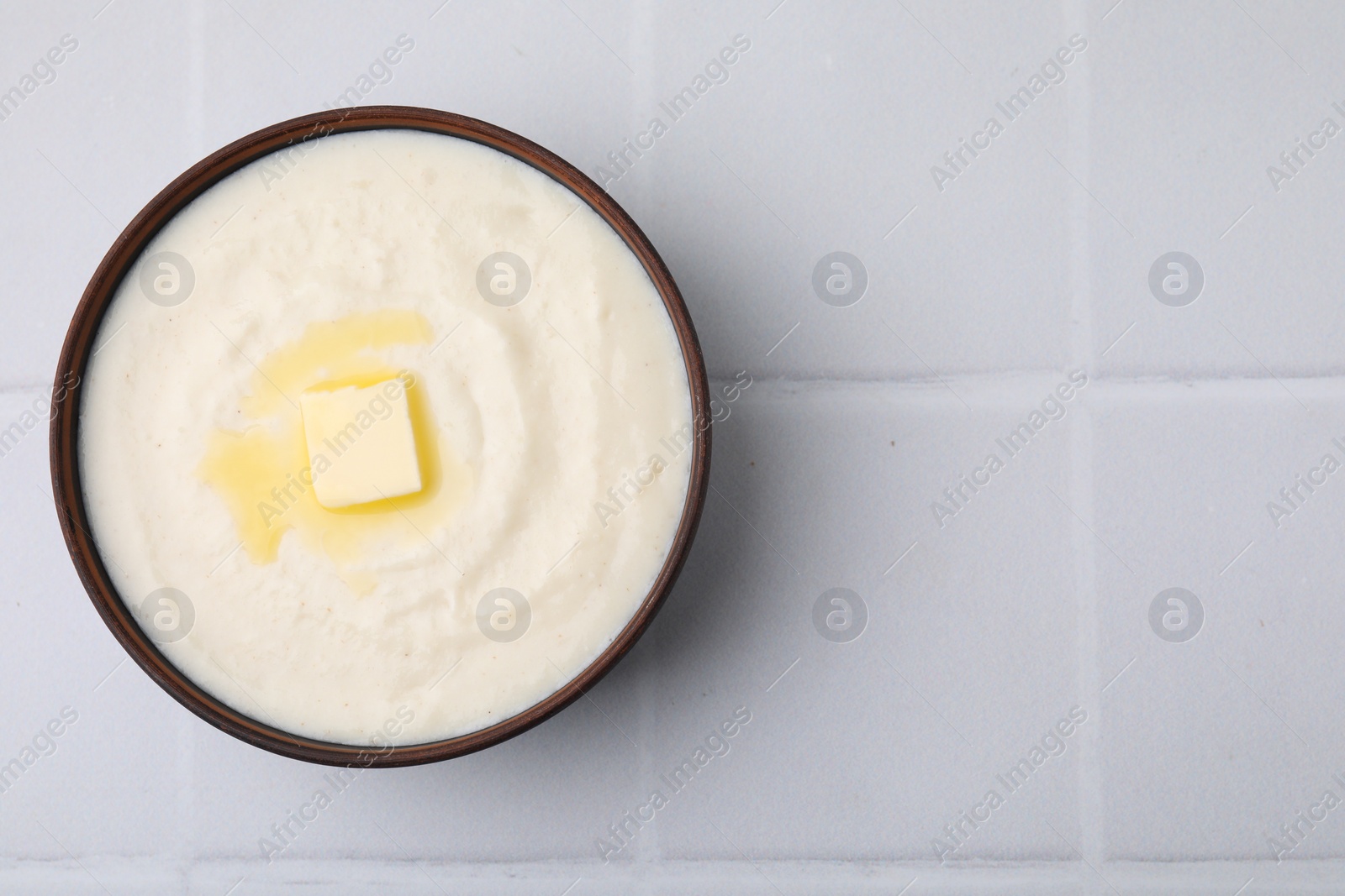 Photo of Delicious semolina pudding with butter in bowl on white tiled table, top view. Space for text