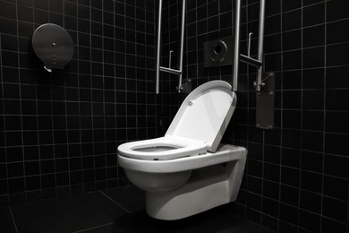 Clean ceramic toilet bowl and handrails on tiled wall indoors