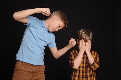 Boy with clenched fists bullying scared kid on black background