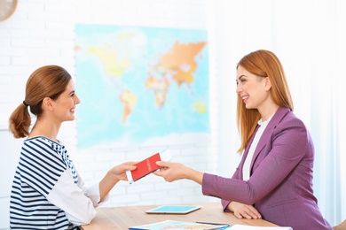 Female manager giving passport with ticket to client in travel agency