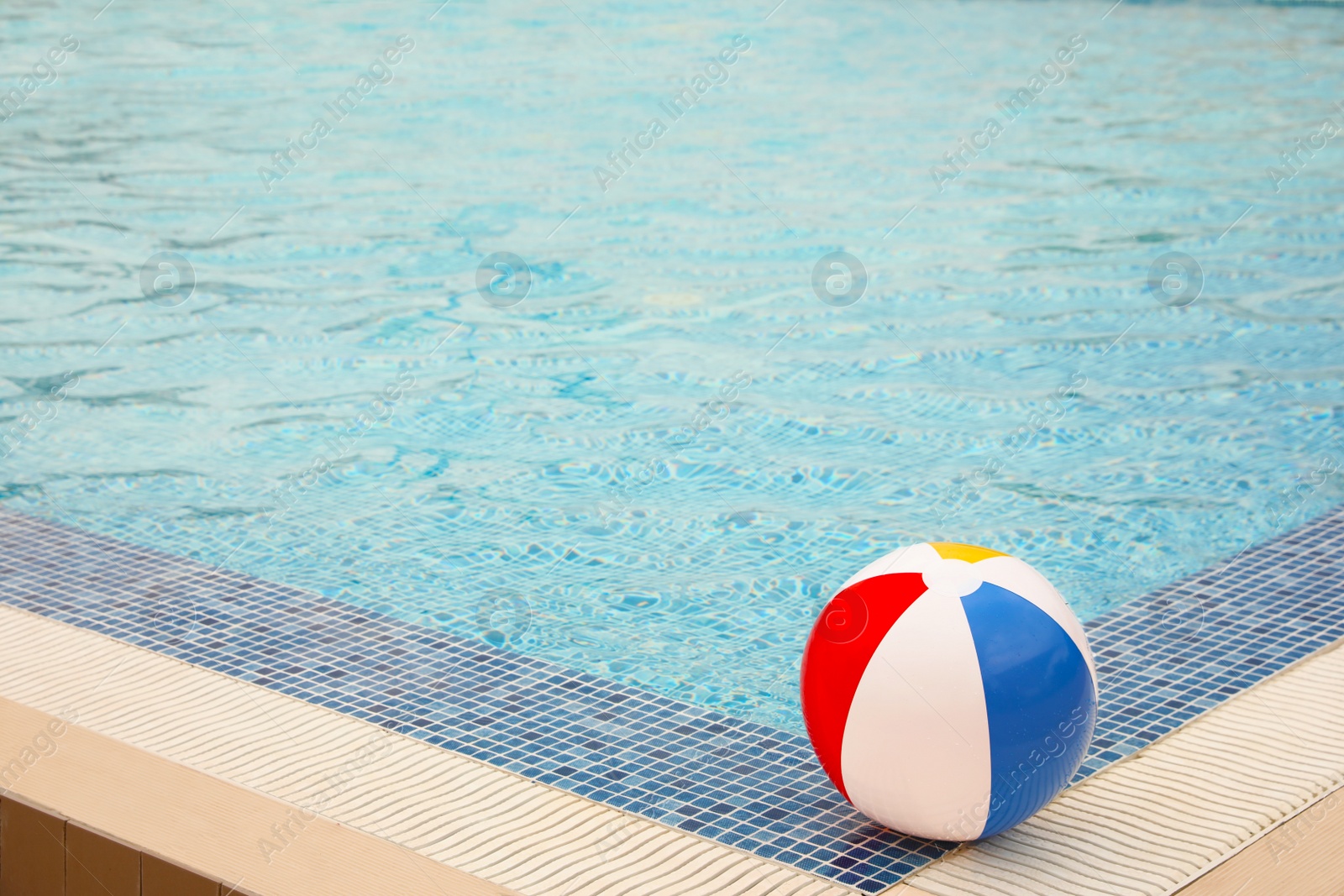 Photo of Inflatable colorful beach ball on edge of outdoor swimming pool, space for text