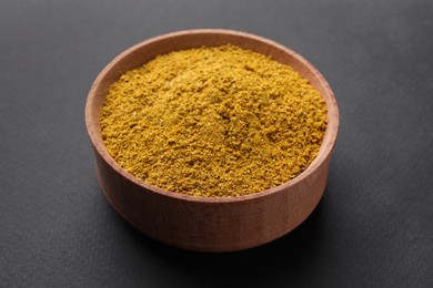 Photo of Aromatic turmeric powder in wooden bowl on dark background