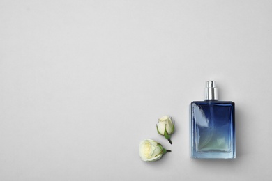 Photo of Bottle of perfume and roses on light background, top view