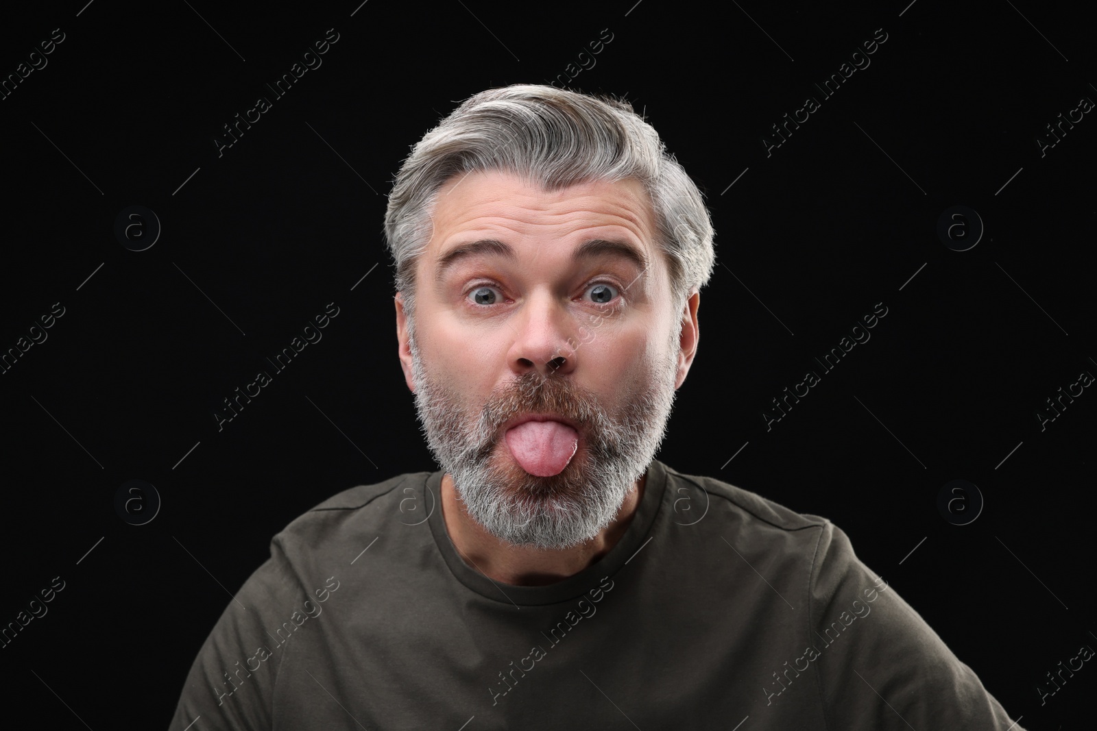 Photo of Personality concept. Bearded man showing tongue on black background
