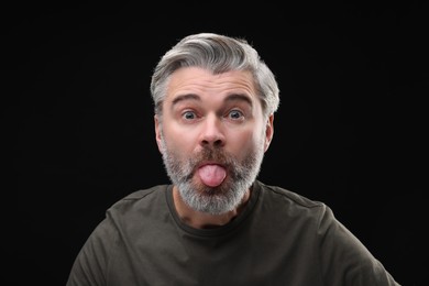 Photo of Personality concept. Bearded man showing tongue on black background