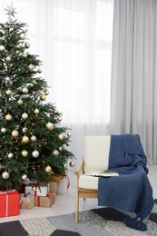 Photo of Beautiful Christmas tree with festive lights, gifts and armchair in living room. Interior design