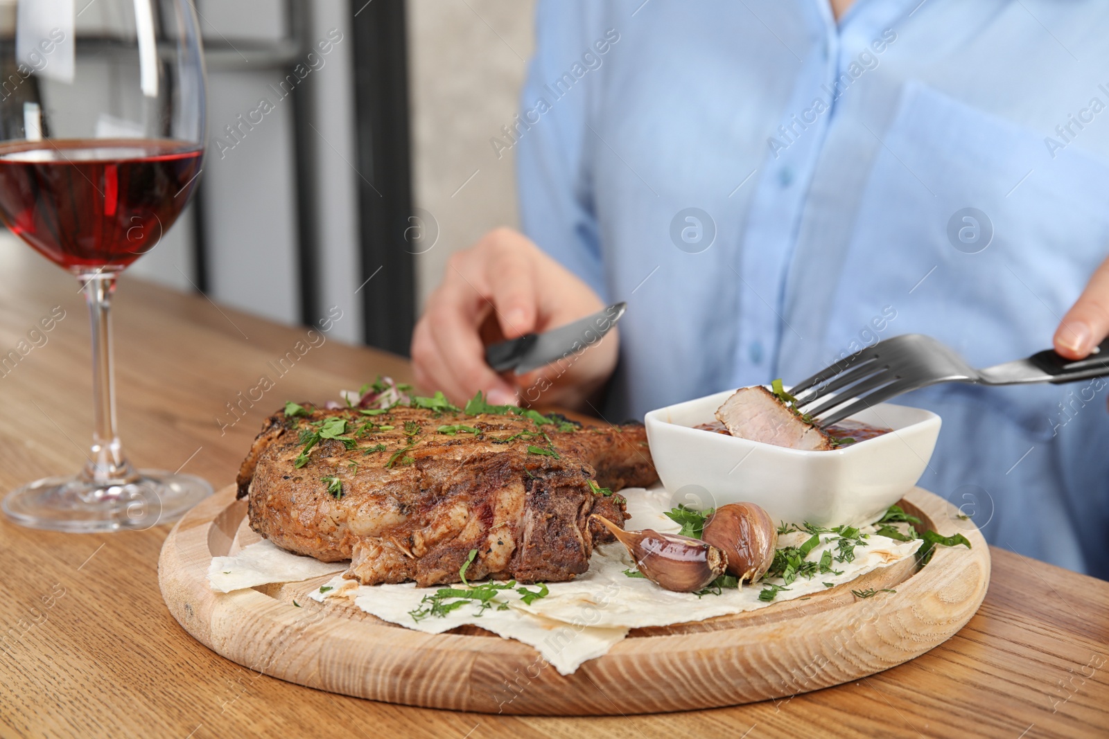 Photo of Woman eating delicious grilled pork chop at wooden table indoors, closeup