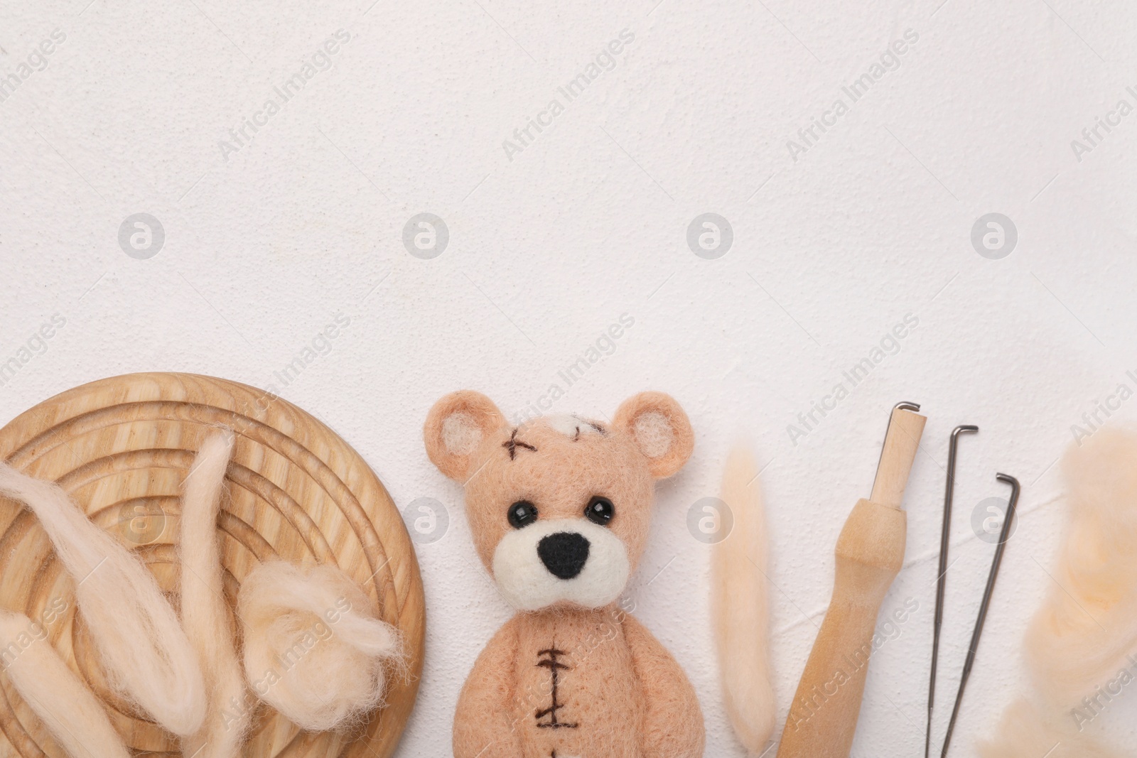 Photo of Felted bear, wool, needles and holder on white table, flat lay. Space for text