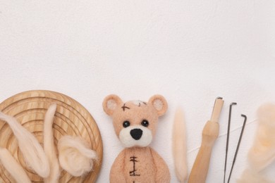 Photo of Felted bear, wool, needles and holder on white table, flat lay. Space for text