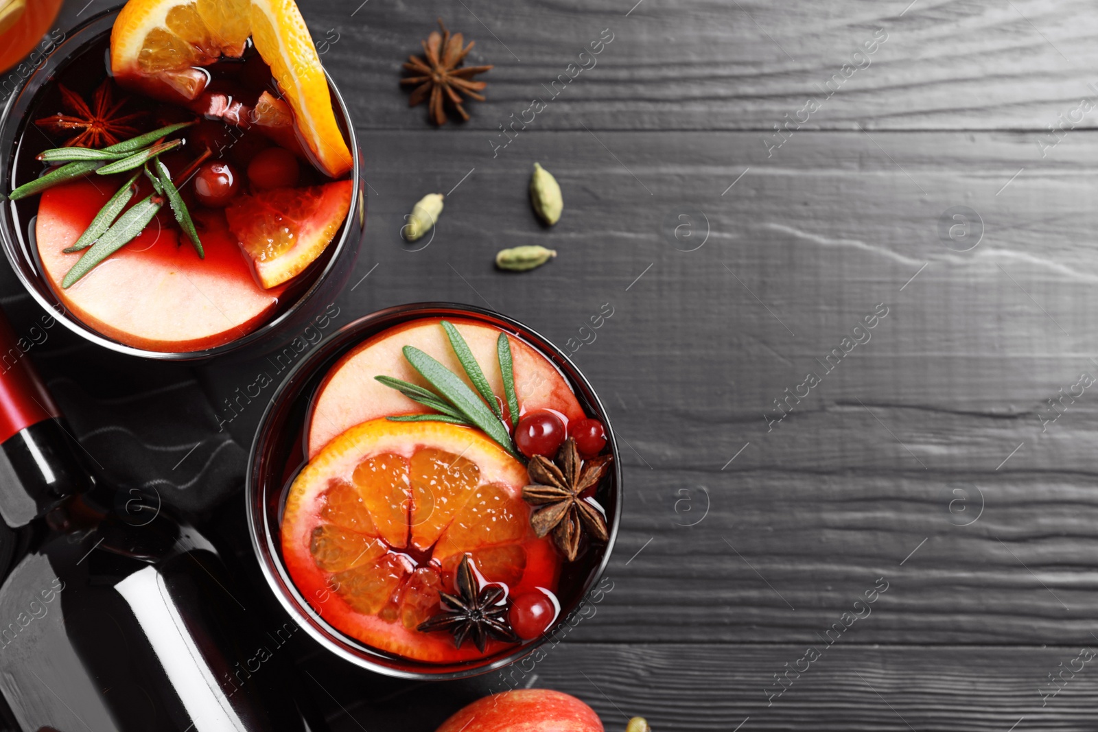 Photo of Cups of tasty mulled wine on black wooden table, flat lay. Space for text