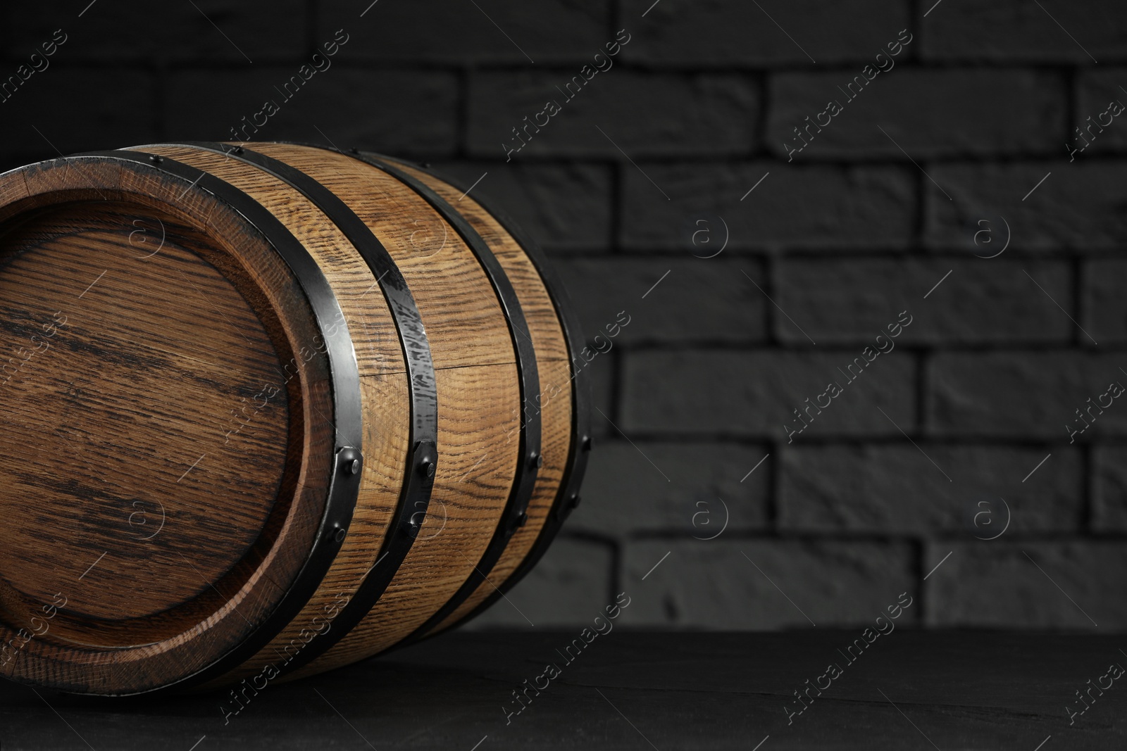 Photo of One wooden barrel on table near brick wall, closeup. Space for text