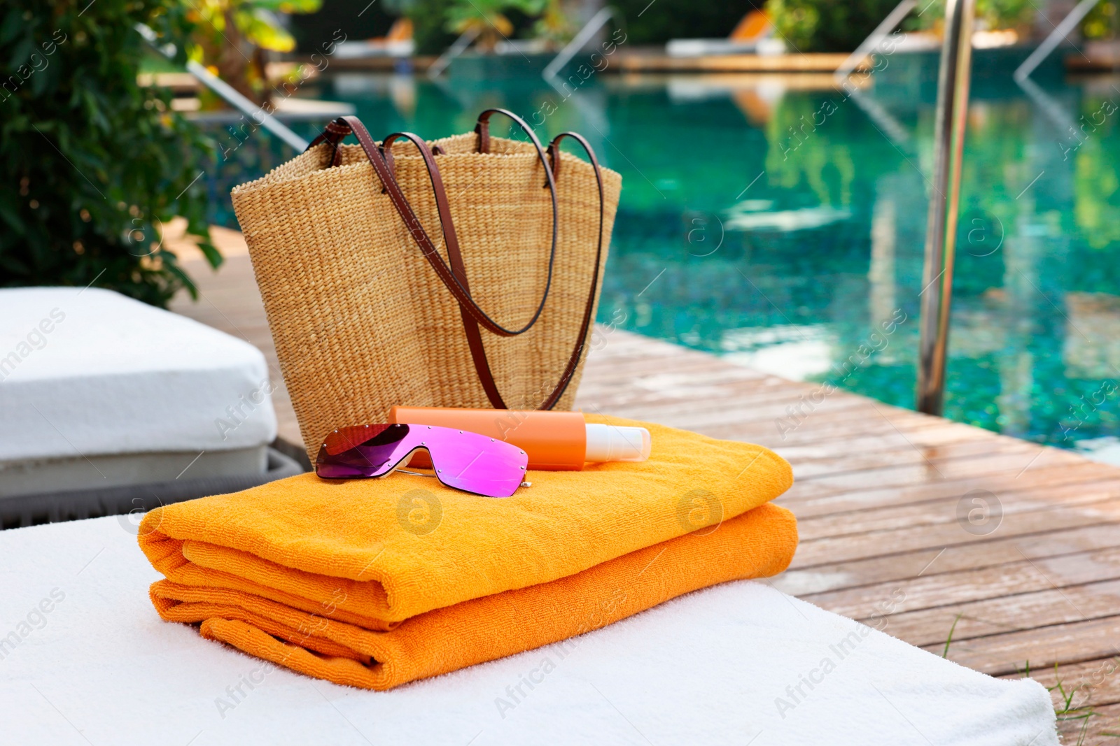 Photo of Wicker bag and beach accessories on sunbed near outdoor swimming pool. Luxury resort