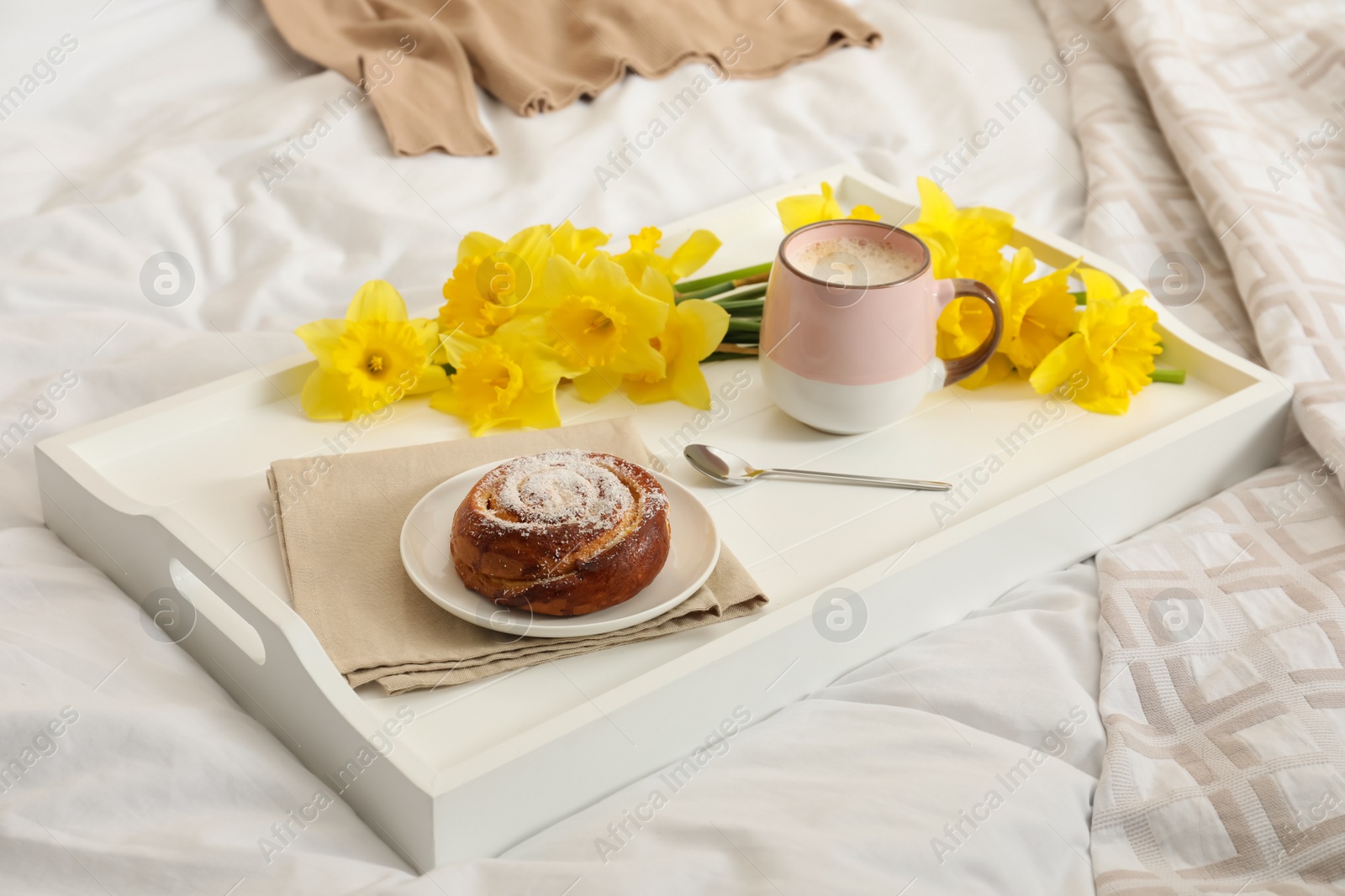 Photo of Bouquet of beautiful daffodils, bun and coffee on bed