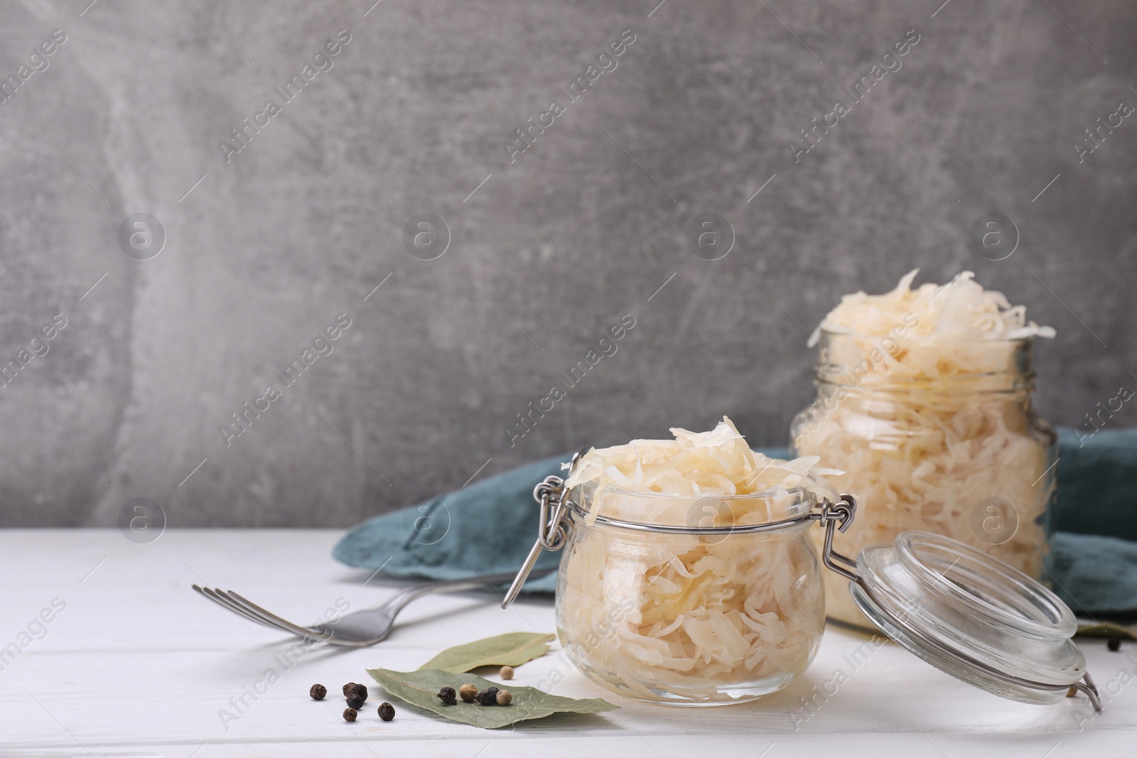 Photo of Glass jars with tasty sauerkraut on white wooden table, space for text