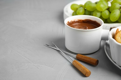 Photo of Fondue pot with chocolate and grape on grey table, space for text