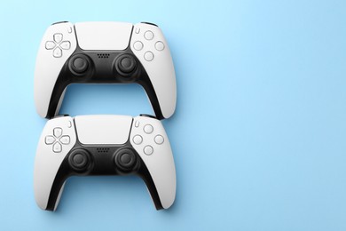 Photo of Wireless game controllers on light blue background, flat lay. Space for text