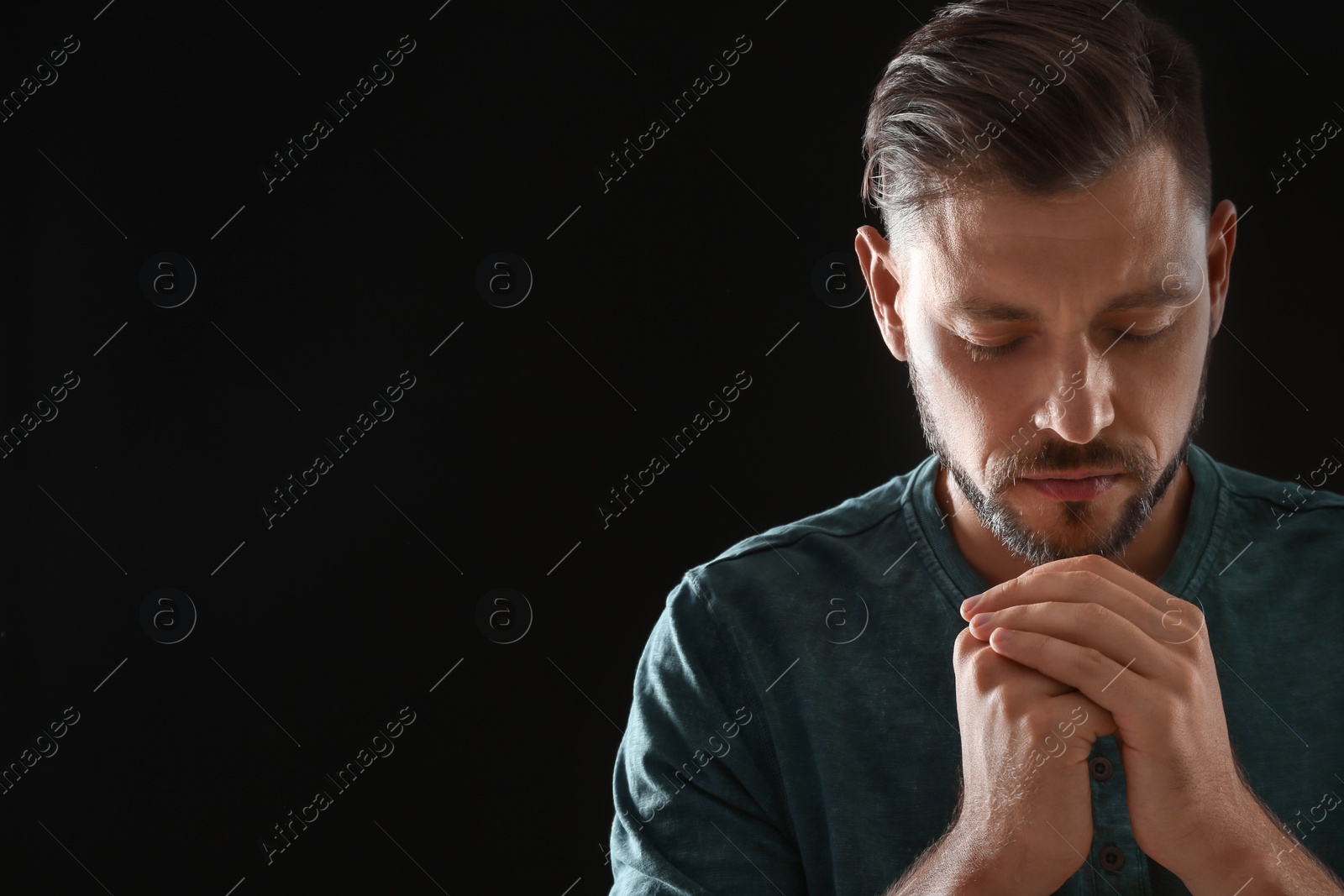 Photo of Man with hands clasped together for prayer on black background. Space for text