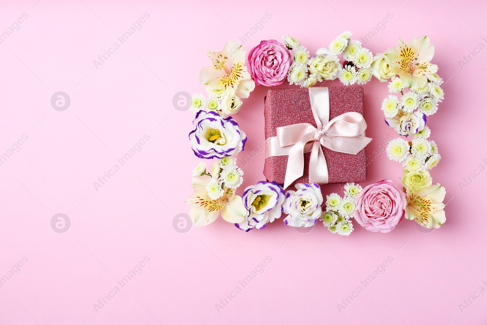 Photo of Frame of flowers and gift box on color background, top view. Space for text