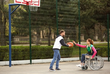 Photo of Woman in wheelchair and young man playing basketball on sports ground