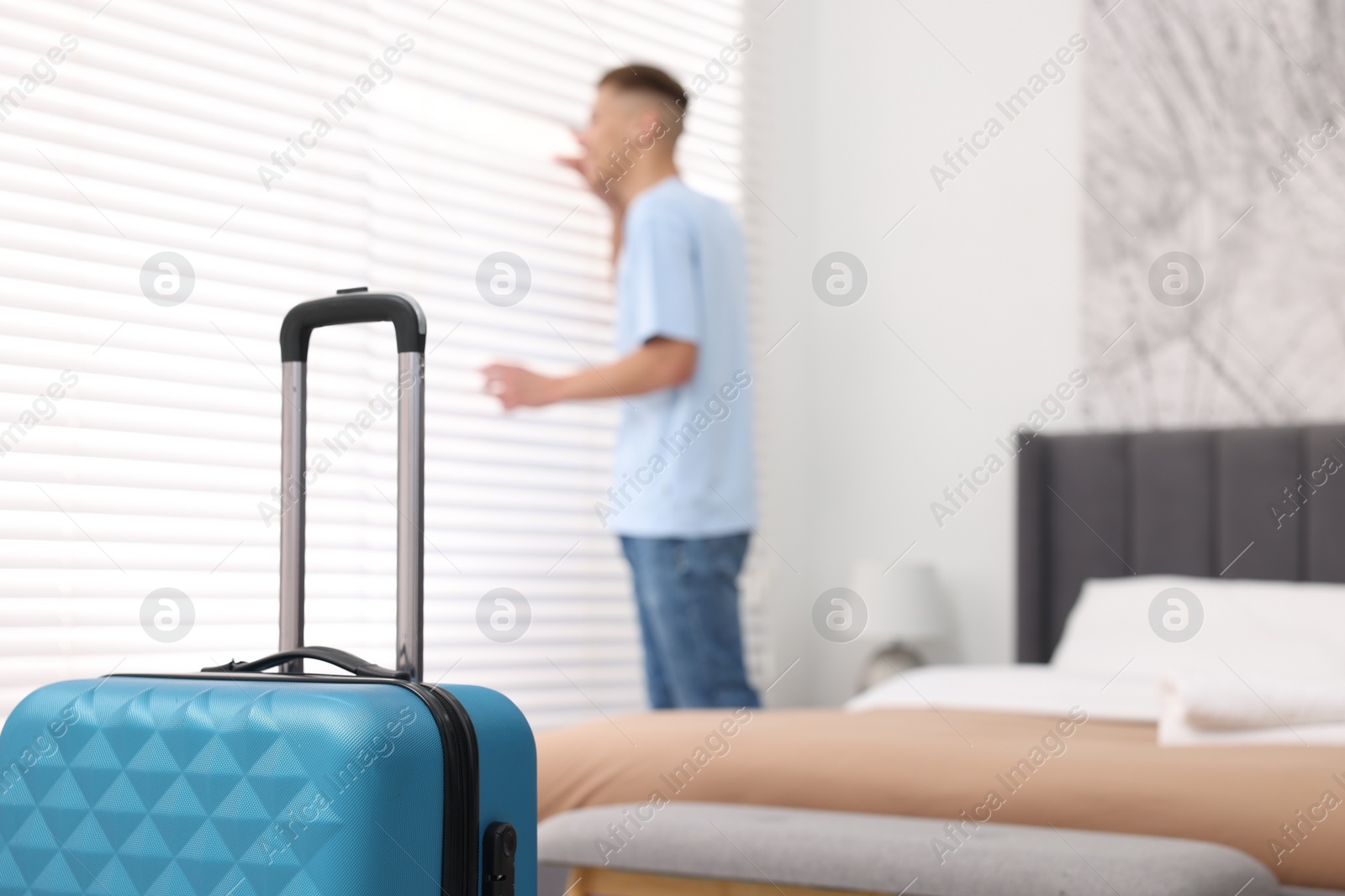 Photo of Guest looking through blinds in stylish hotel room, focus on suitcase