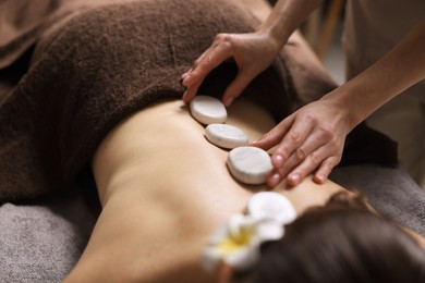 Spa therapy. Beautiful young woman lying on table during hot stone massage in salon, closeup