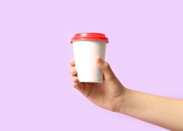 Photo of Woman holding takeaway paper coffee cup on violet background, closeup