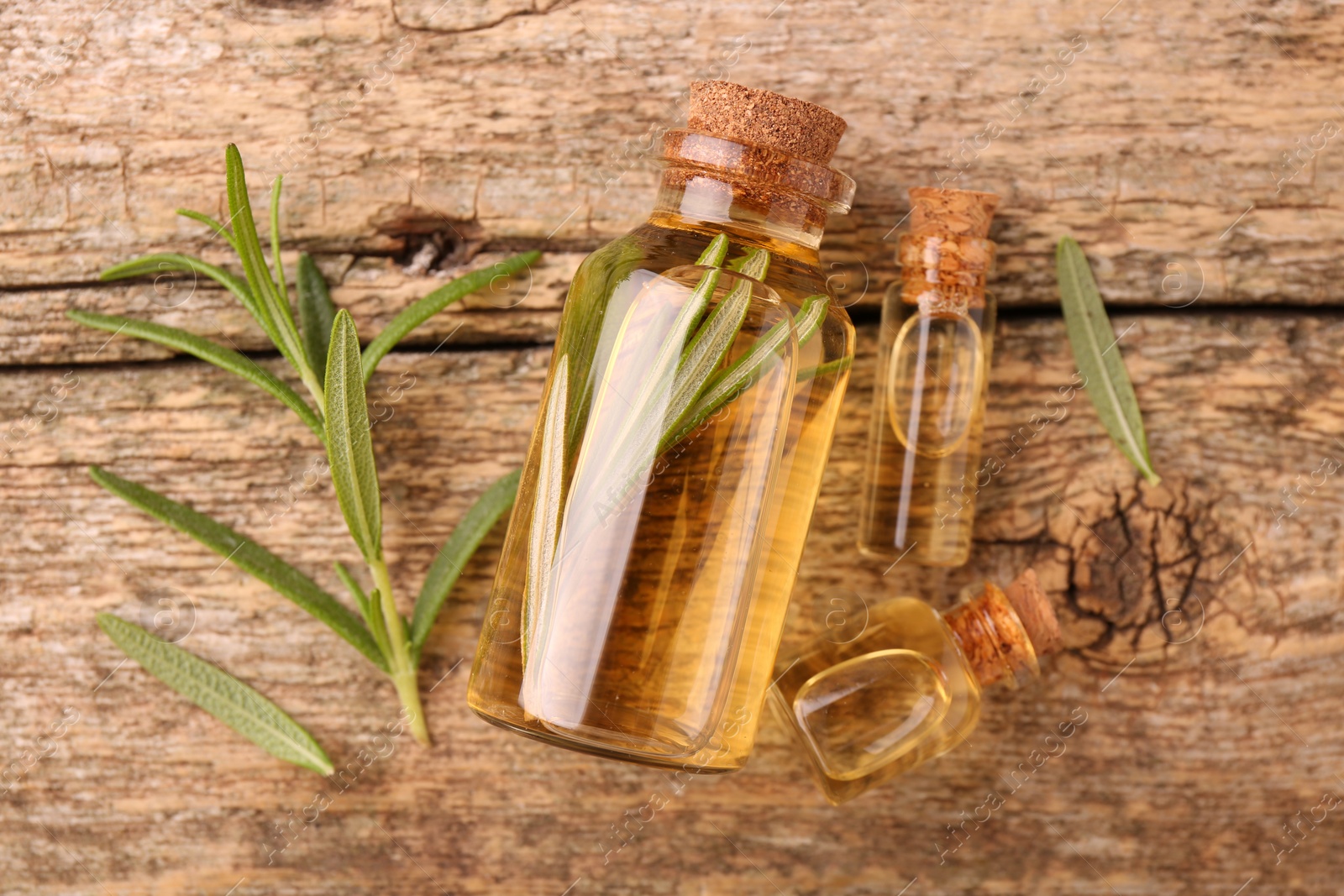 Photo of Aromatic essential oils in bottles and rosemary on wooden table, flat lay